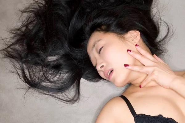 Mulher de olhos fechados deitada na cama tendo um orgasmo - Metrópoles