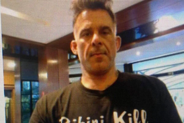 Homem branco sem barba e cabelo curto usando camiseta preta com os dizeres "bikini kill" - Metrópoles