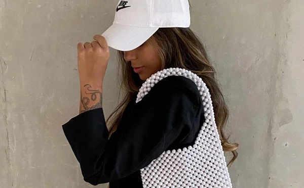 Modelo usa boné branco da marca nike e usa também uma bolsa branca de miçangas - Metrópoles