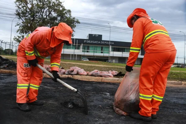 Servidores do SLU fazem a limpeza de asfalto queimado após manifestações de bolsonaristas na Asa Norte do dia de ontem. Na imagem, dois garis limpam local próxima à 5º Delegacia de Polícia Civil do DF - Metrópoles