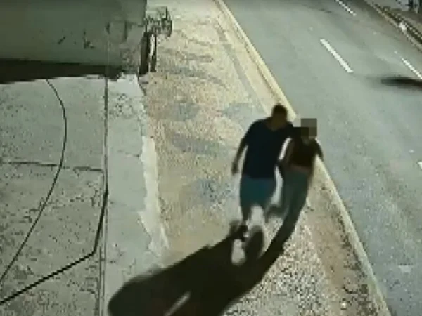 Foto colorida mostra duas pessoas caminhando por calçada