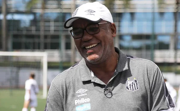 foto colorida mostra Serginho Chulapa usando boné branco do Santos, camiseta escura do clube, óculos e sorrindo - Metrópoles