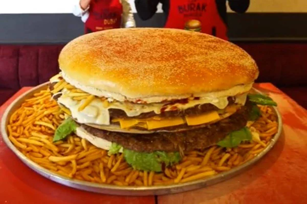 Na foto, um homem posa em frente a um hambúrguer gigante com uma criança do lado