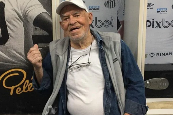 Silvio Luiz posa, sorridente, no vestiário de um estádio ao lado de fotos de jogadores - Metrópoles