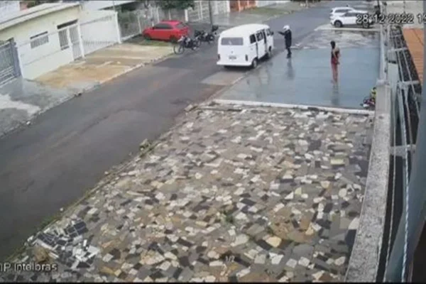 Imagem colorida de uma rua na cidade de Taguatinga-DF, onde há uma kombi branca com policiais apontando para sua direção