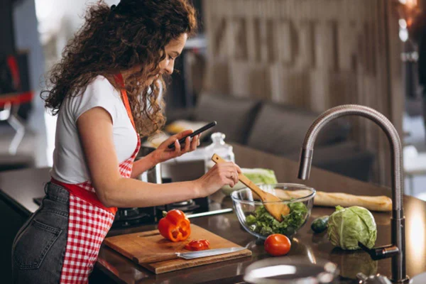 Mulher cozinhando com celular na mão
