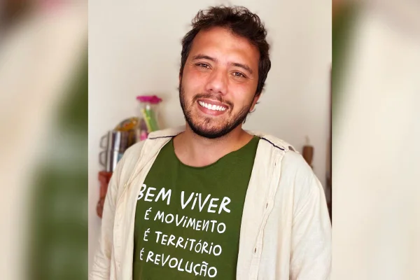 Foto de um homem sorrindo com camisa verde e casaco bege por cima
