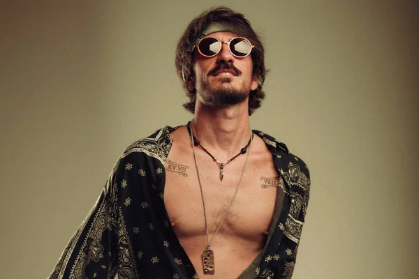 homem com camisa aberta oculos redondos e bandana no cabelo que vai até o queixo - metrópoles