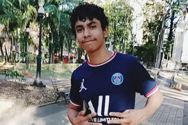 Adolescente com pele morena usa camiseta de time azul e faz sinal com as mãos - Metrópoles