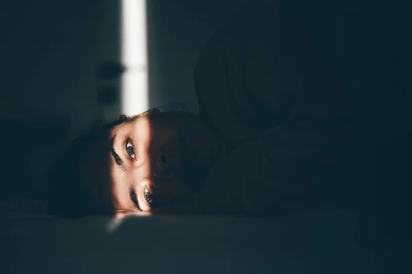 Mulher deitada no escuro. Apenas uma listra de luz passa por seus olhos - Metrópoles
