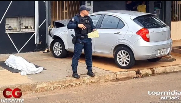 Foto colorida de oilicial ao lado do corpo do idoso coberto por um lençol branco - Metrópoles
