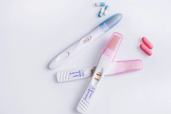 teste de gravidez rosa e teste de gravidez azul com alguns comprimidos ao lado - Metrópoles