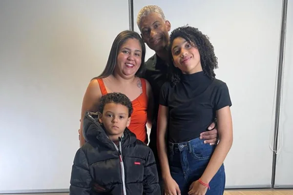 Foto colorida de família reunida, uma criança do sexo masculino, uma menina adolescente, pai e mãe abraçados. - Metrópoles.