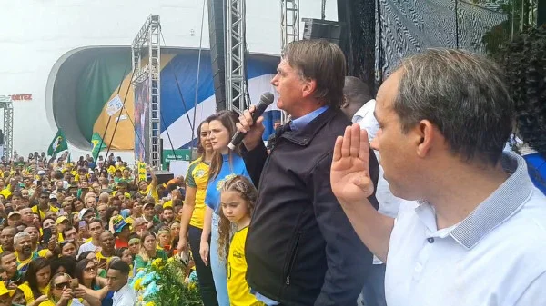 Bolsonaro discursa no Rio de Janeiro diante de plateia vestida de verde e amarelo e ataca PT. Ele segura microfone e usa jaqueta preta - Metrópoles