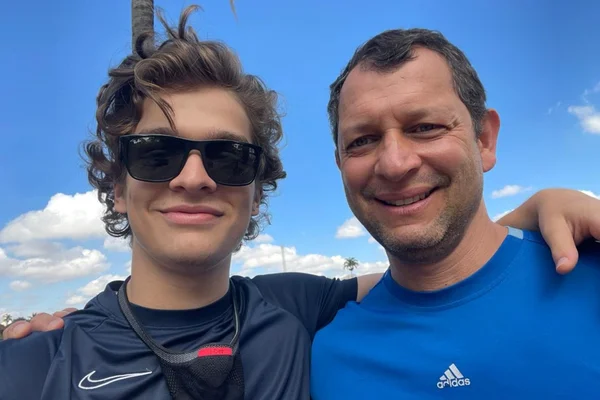 Menino com óculos escuro abraçado com homem com camisa azul