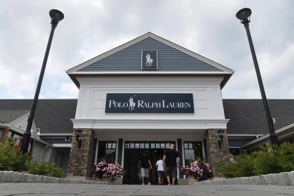 Fachada da loja da Ralph Lauren. O estabelecimento fica em um shopping ao céu aberto, provavelmente um outlet. É possível ver pessoas entrando no recinto.