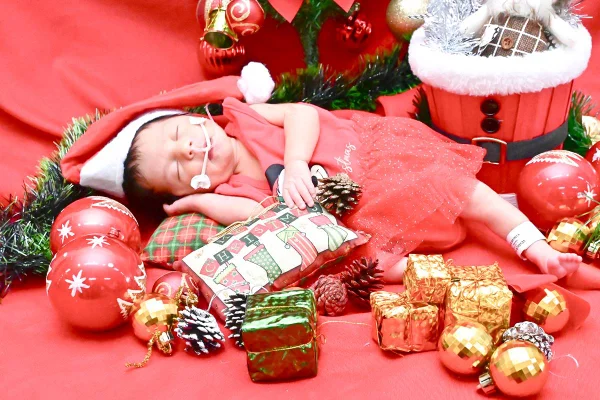 Foto colorida de bebê internado em ensaio fotográfico, com roupas de natal