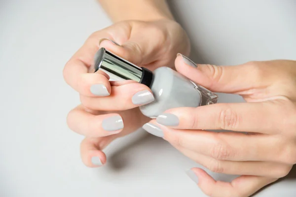 mãos com unhas pintadas de cinza segurando um esmalta cinza