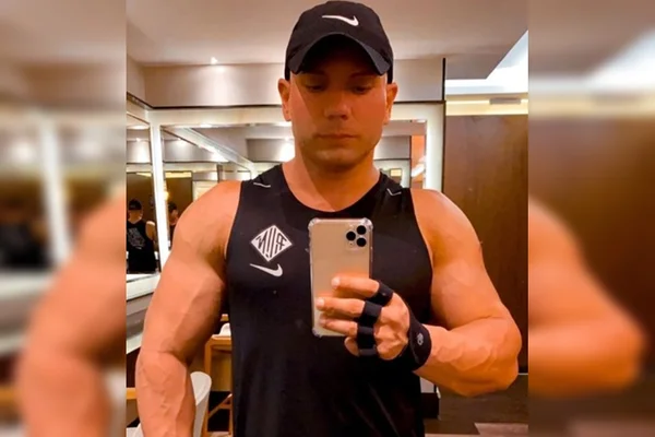Homem musculoso com regata preta e boné preto tirando foto no espelho