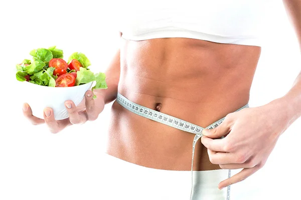 Imagem colorida mostra uma mulher com um prato de salada na mão e uma fita métrica na outra - Metrópoles