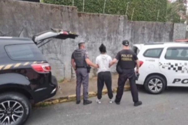 Imagem colorida mostra mulher sendo segurada pelos braços por dois policiais fardados. Os três estão de costas - Metrópoles