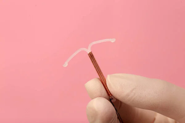 Foto colorida de uma mão com luvas brancas segurando um diu de cobre em um fundo cor-de-rosa - Metrópoles