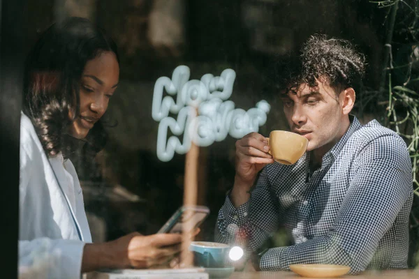 Mulher à mesa ao lado de homem bebendo café - Metrópoles