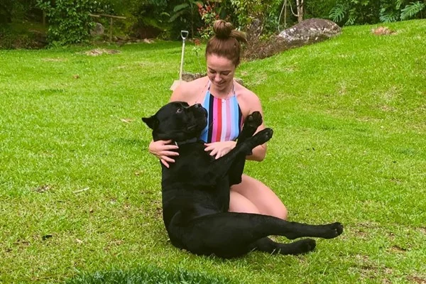 De maiô cavado, Paolla Oliveira rola na grama com cachorro