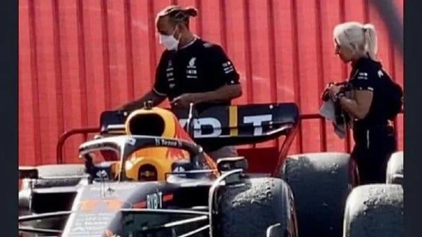 Imagem colorida de Lewis Hamilton passando atrás do carro da red bull