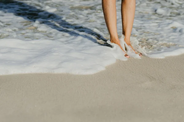 Pernas de pessoa tocando o mar em areia da praia - Metrópoles