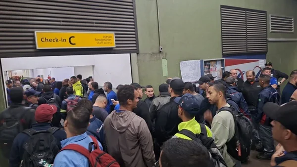 Em foto colorida pessoas aglomerada em frente de placa amarela - Metrópoles