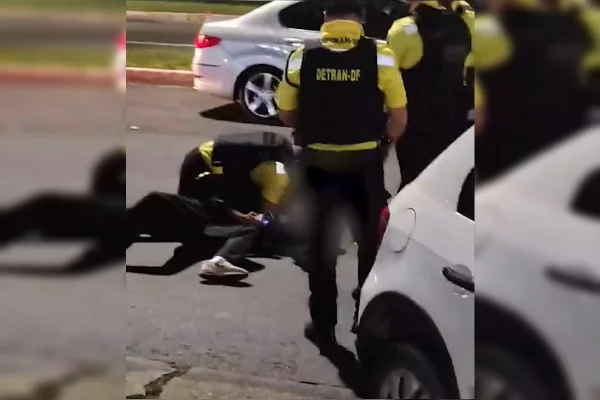 Imagem de cinco agentes do Detran-DF, vestidos de farda amarela e preta, ao redor de um carro branco