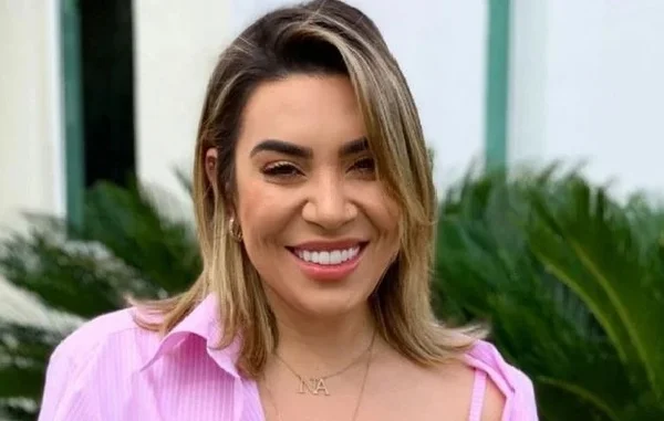 Na imagem colorida, uma mulher está posicionada no centro. Ele tem cabelos curtos e loiros e está sorrindo para a camera