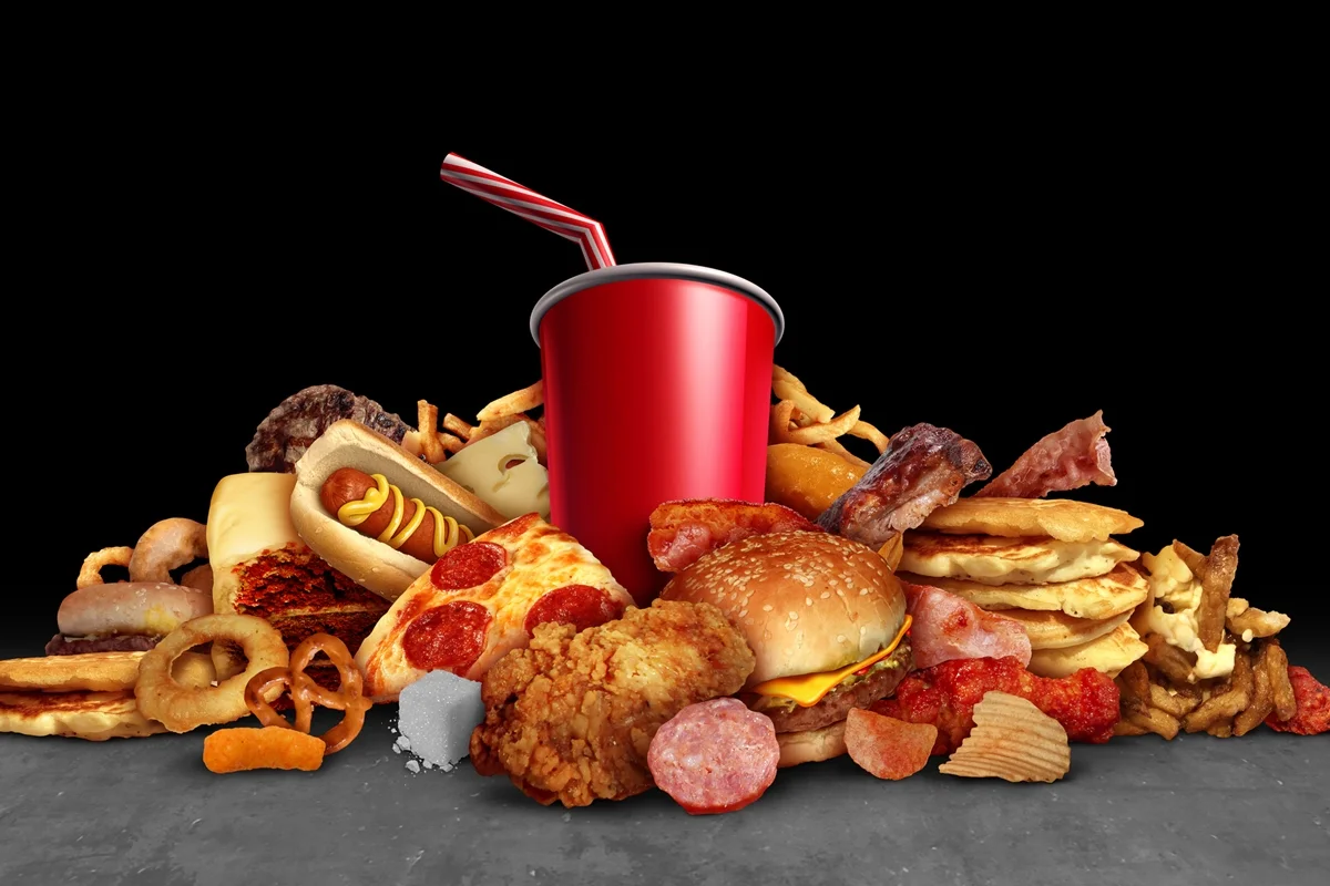 Alimentos processados e calóricos, como frituras, hambúrgueres e refrigerantes, que acarretam riscos à saúde como obesidade e diabetes, devido ao alto teor de gorduras prejudiciais à saúde, em um fundo preto com elementos de ilustração 3D. Metrópoles