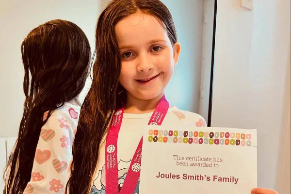 foto colorida de menina pequena, branca de cabelos longos castanhos segurando certificado - metrópoles