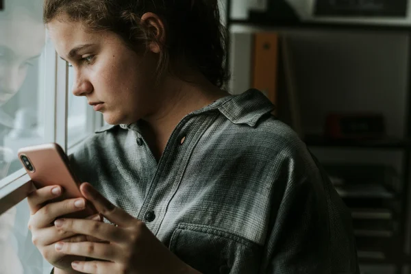 Garota adolescente segurando um celular. Conceito de depressão por uso excessivo de redes sociais. Metrópoles