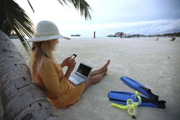 imagem colorida com mulher na praia olhando para computador em home office