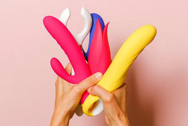 Pessoa segura diversos sex toys coloridos sob fundo rosa - Metrópoles