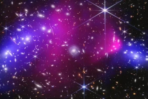 Imagem do Espaço que mostra o Bullet Cluster. Estrelas em volta de poeira cómica das cores roxo e rosa. - Metrópoles