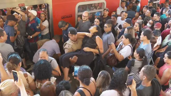 Imagem de multidão em plataforma de trem; uma mulher desmaiada é socorrida por bombeiro - Metrópoles