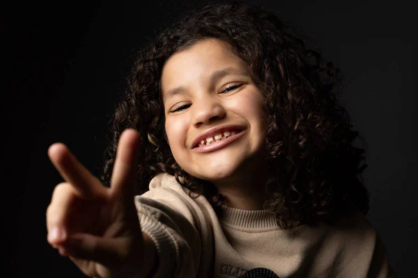 menina faz numero 2 com os dedos e sorri - metrópoles