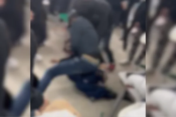 Imagem colorida e borrada de aluno em cima de outro o agredindo com socos e chutes. Metrópoles