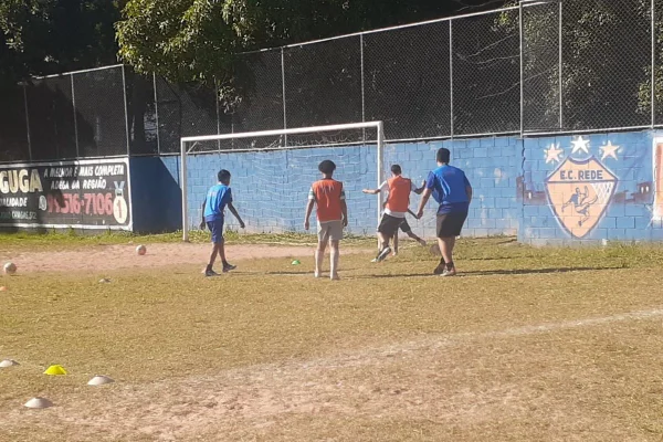 Imagem colorida mostra crianças jogando futebol em campo gramado - Metrópoles