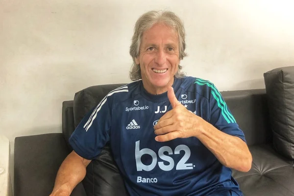 Fotografia de Jorge Jesus com o uniforme do Flamengo posando para foto sorrindo e dando sinal de positivo com a mão
