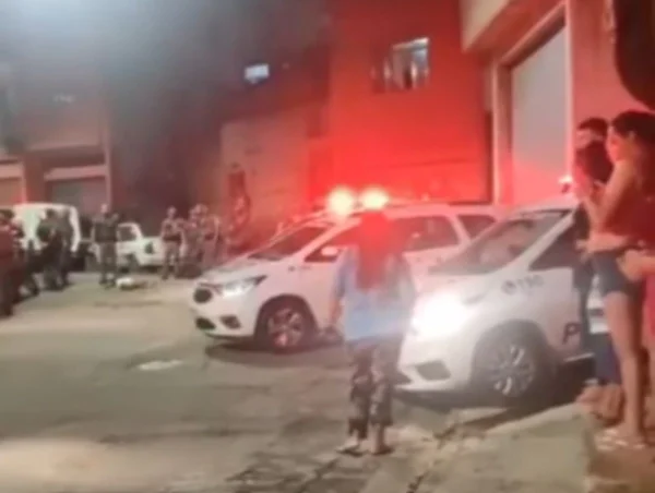 Foto colorida tirada à noite mostra viaturas da PM estacionadas com sirenes ligadas e PMs ao fundo