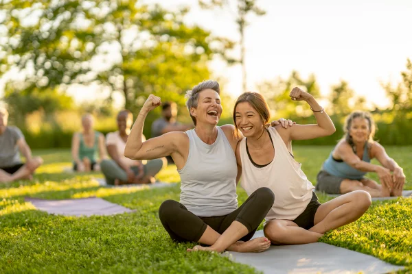 Foto de duas mulheres sentadas em gramado abraçadas e sorrindo - Metrópoles