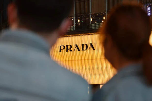 A imagem mostra duas pessoas fotografadas de costas enquanto olham para a loja da Prada