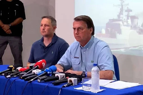 Bolsonaro com deputado Capitão Derrite (PP-SP) em coletiva de imprensa. Ambos estão sentados em mesa com vários microfones, sem máscara - Metrópoles