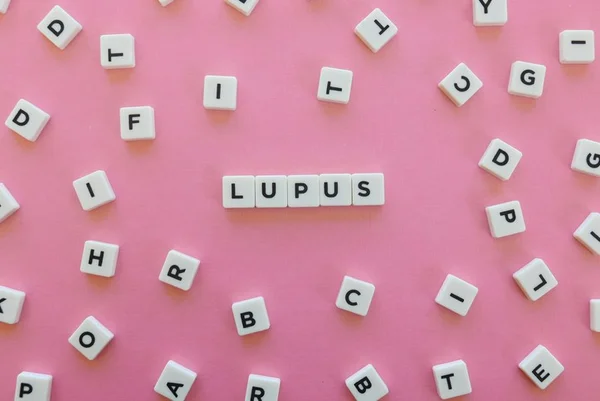blocos de letras de jogo formando a palavra lúpus em fundo rosa - Metrópoles - Lúpus car-t