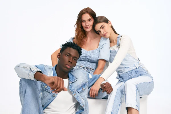 Três modelos - um homem negro e duas mulheres brancas - posam usando looks em jeans